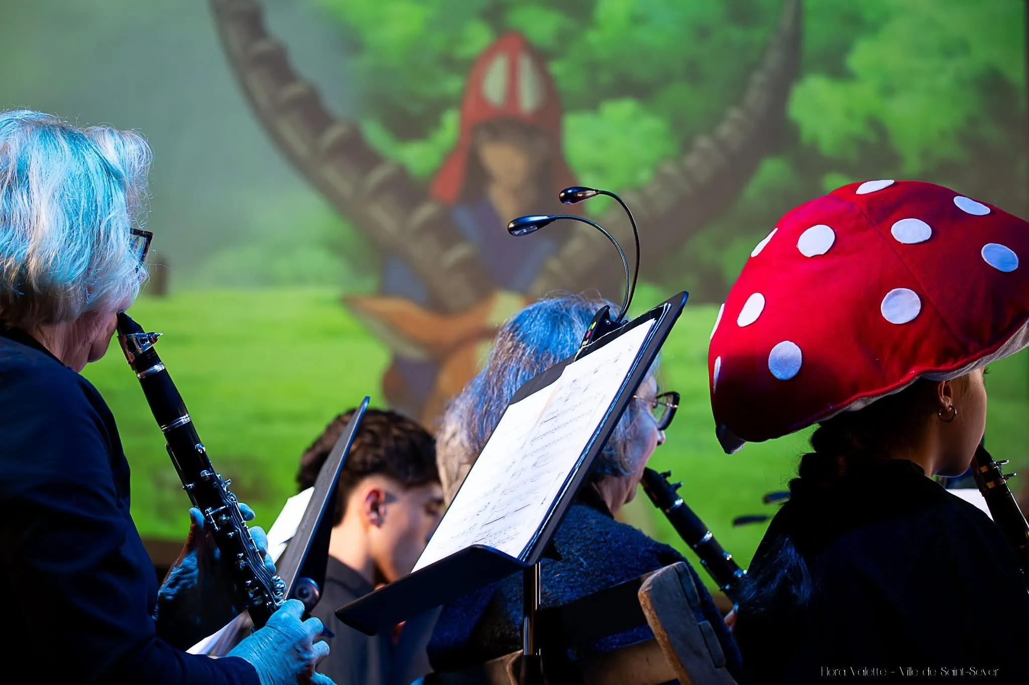 Le pupitre des clarinettes devant une projection de Princesse Mononoké, une musicienne coiffée d'un chapeau champignon au premier plan