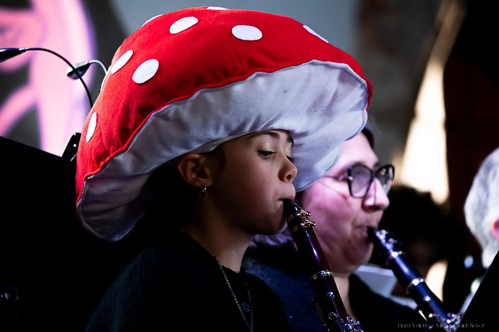 Jeune clarinettiste coiffée d'un grand chapeau champignon rouge à pois blancs, en pleine lecture