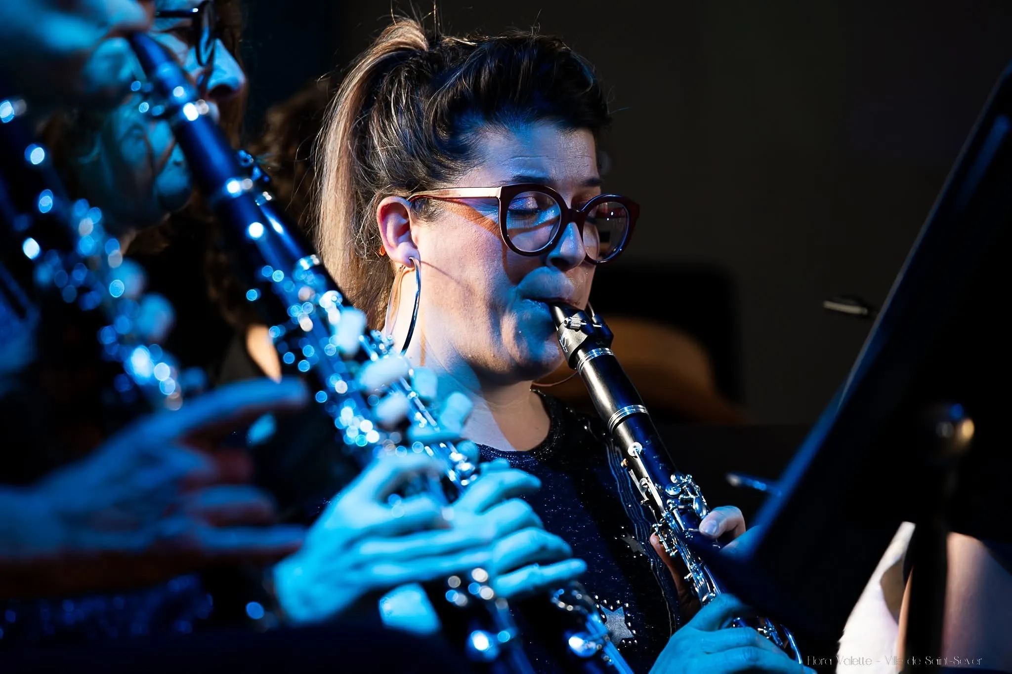 Clarinettiste en gros plan sous une lumière bleue, lunettes rondes et créoles