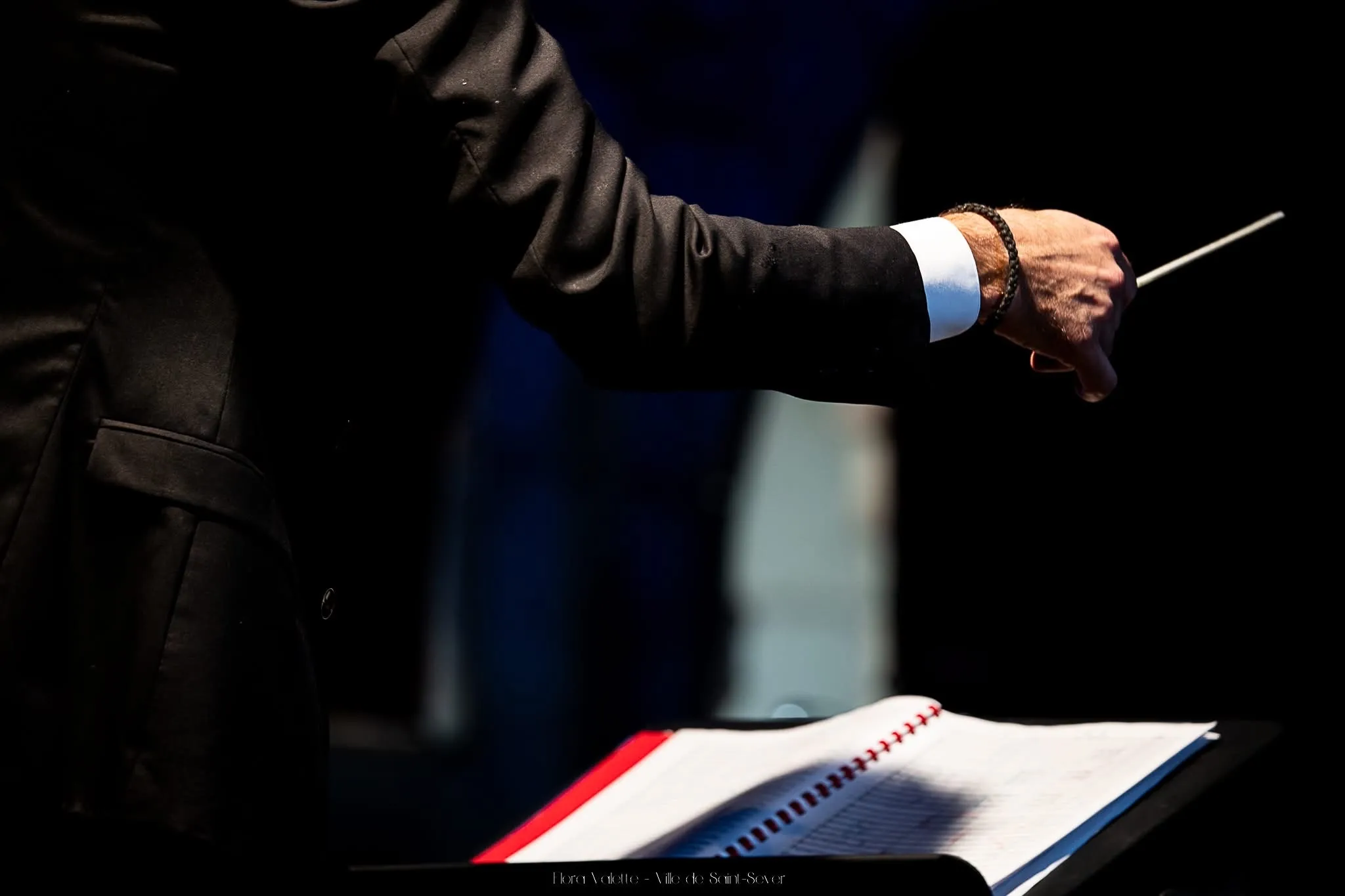 Gros plan sur la main du directeur musical tenant la baguette au-dessus d'une partition ouverte