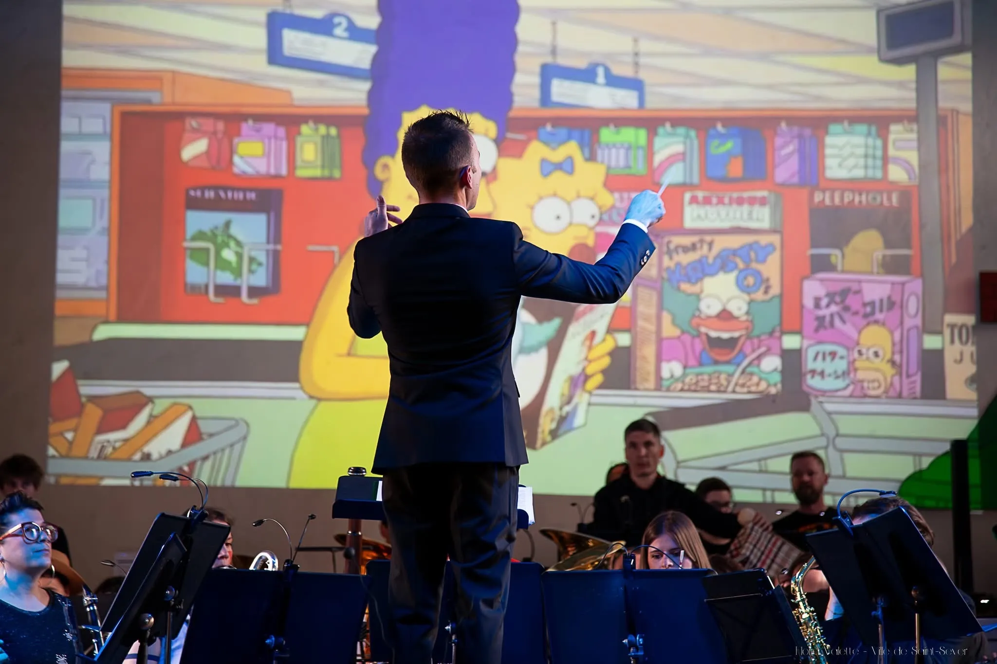 Le chef d'orchestre dirigeant devant une projection géante des Simpson, Marge et Maggie au supermarché