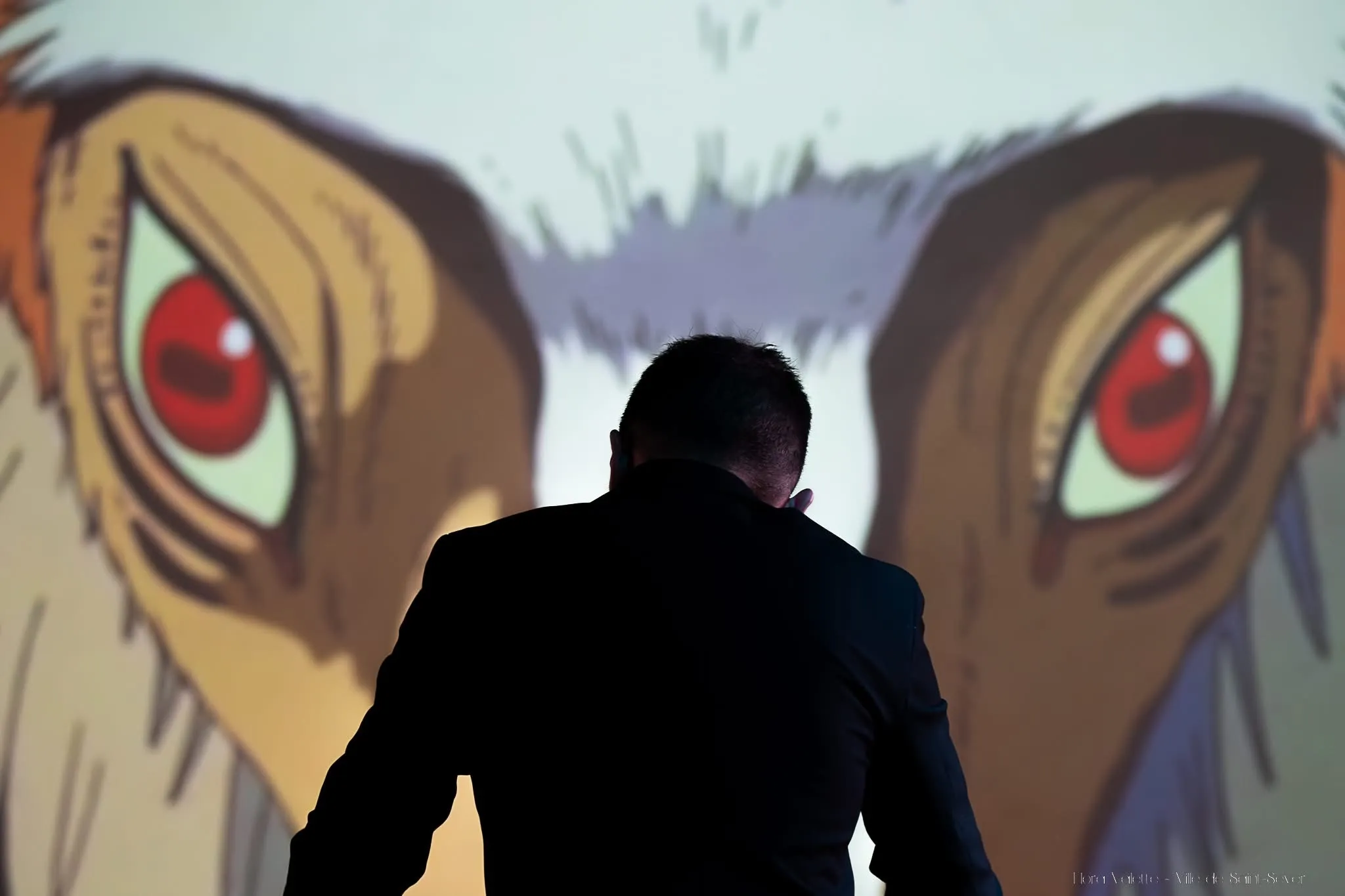 Le chef d'orchestre de dos, face aux yeux géants du loup Moro projetés sur l'écran, extrait de Princesse Mononoké