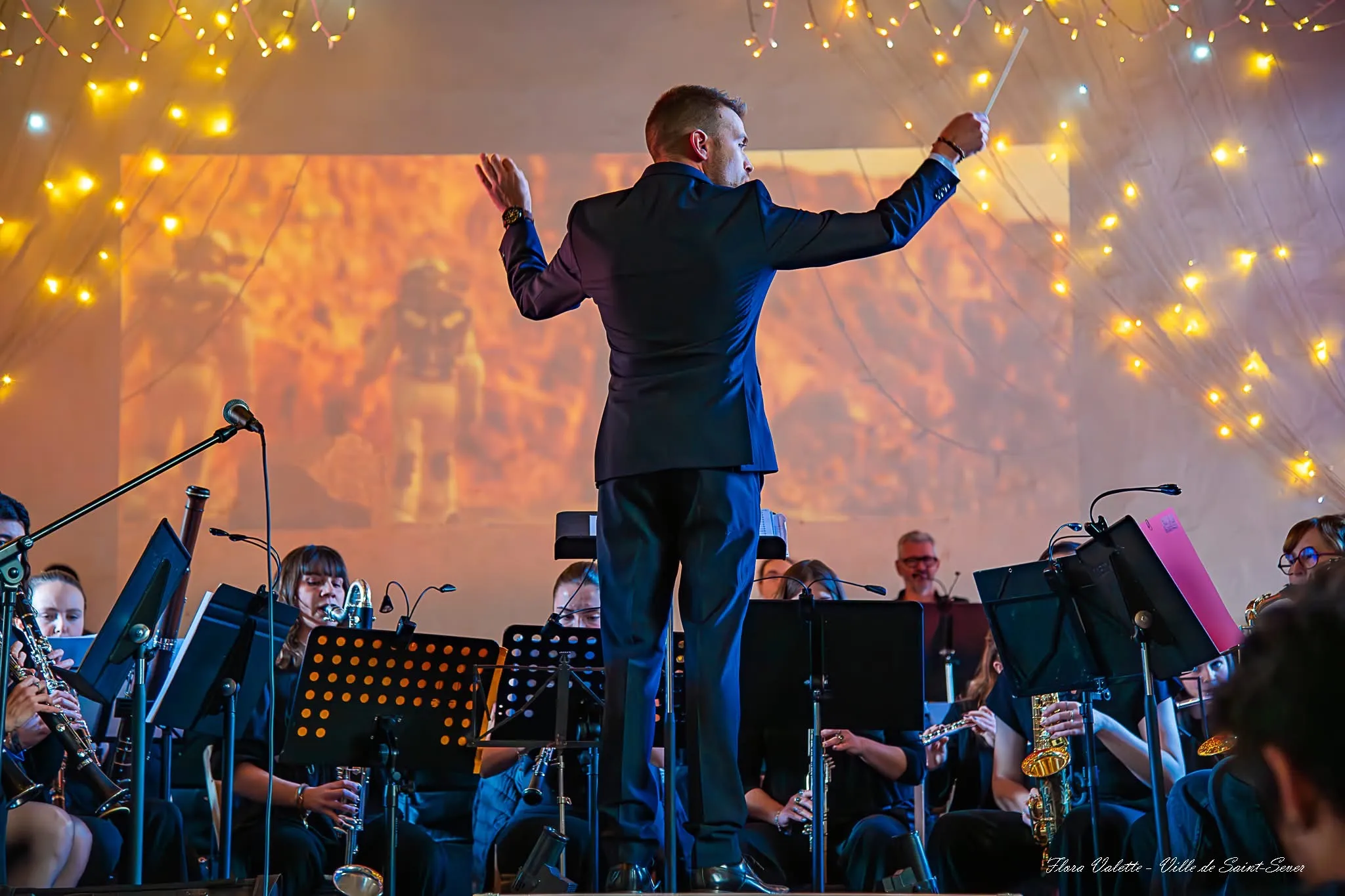 Le directeur musical dirigeant l'orchestre, bras grands ouverts