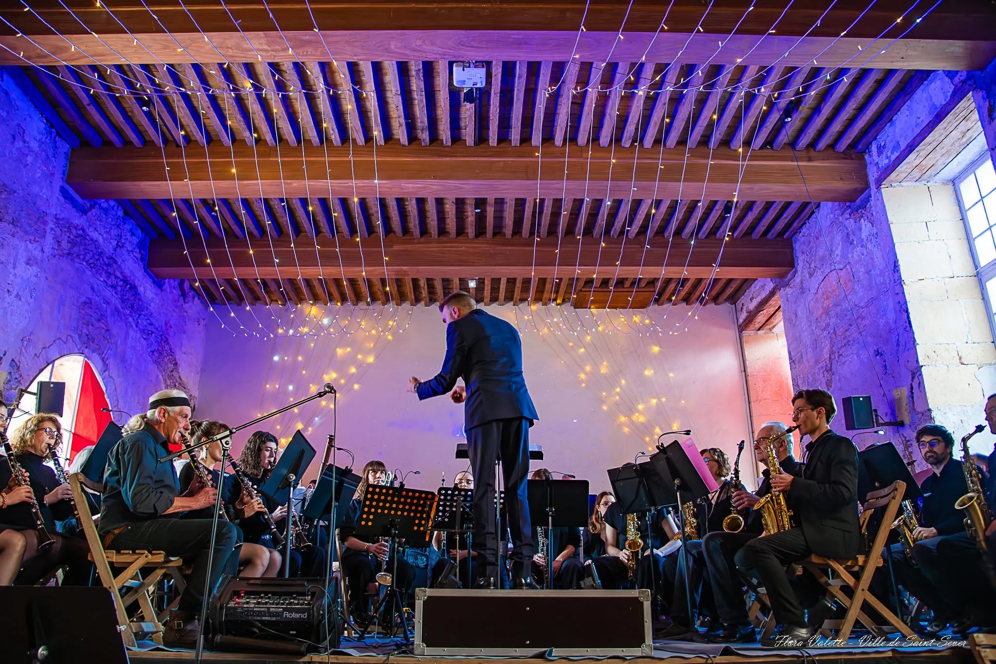 L'Orchestre d'Harmonie du Cap de Gascogne au complet sur la scène du Cloître des Jacobins de Saint-Sever, sous les guirlandes lumineuses tendues à la charpente