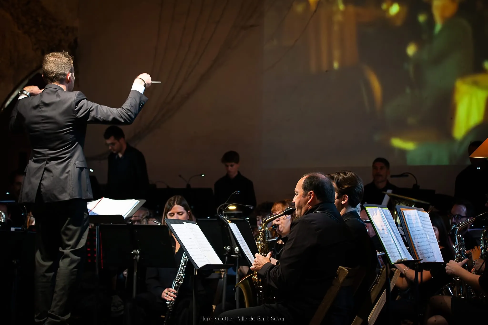Le directeur musical dirigeant l'orchestre devant un grand écran de projection