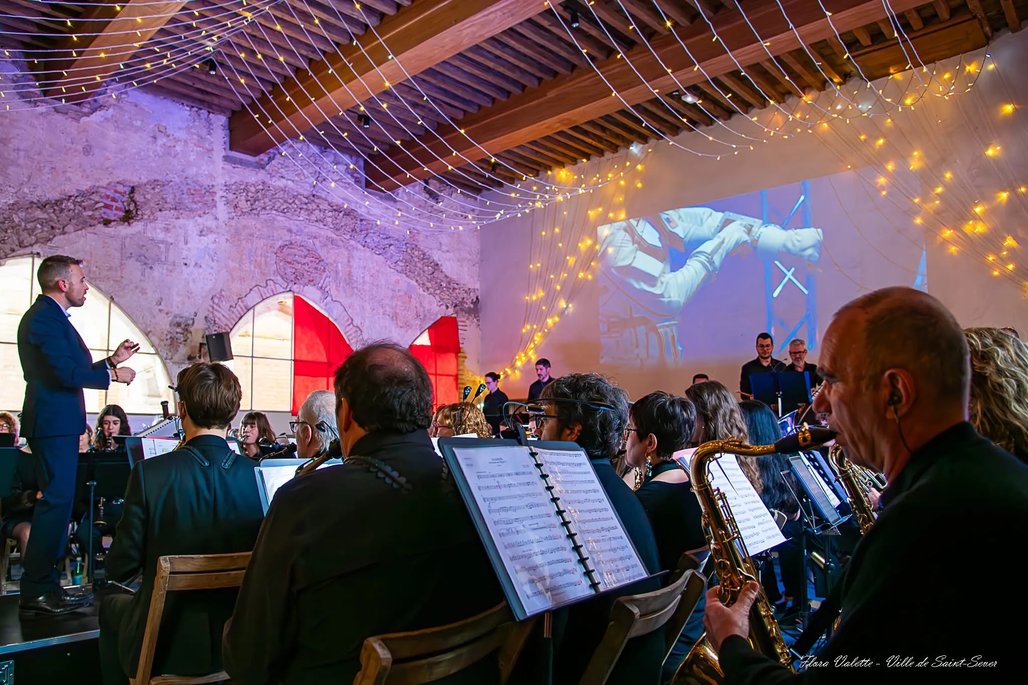 Vue depuis les pupitres de l'orchestre : partitions au premier plan, le directeur et l'écran de projection au fond