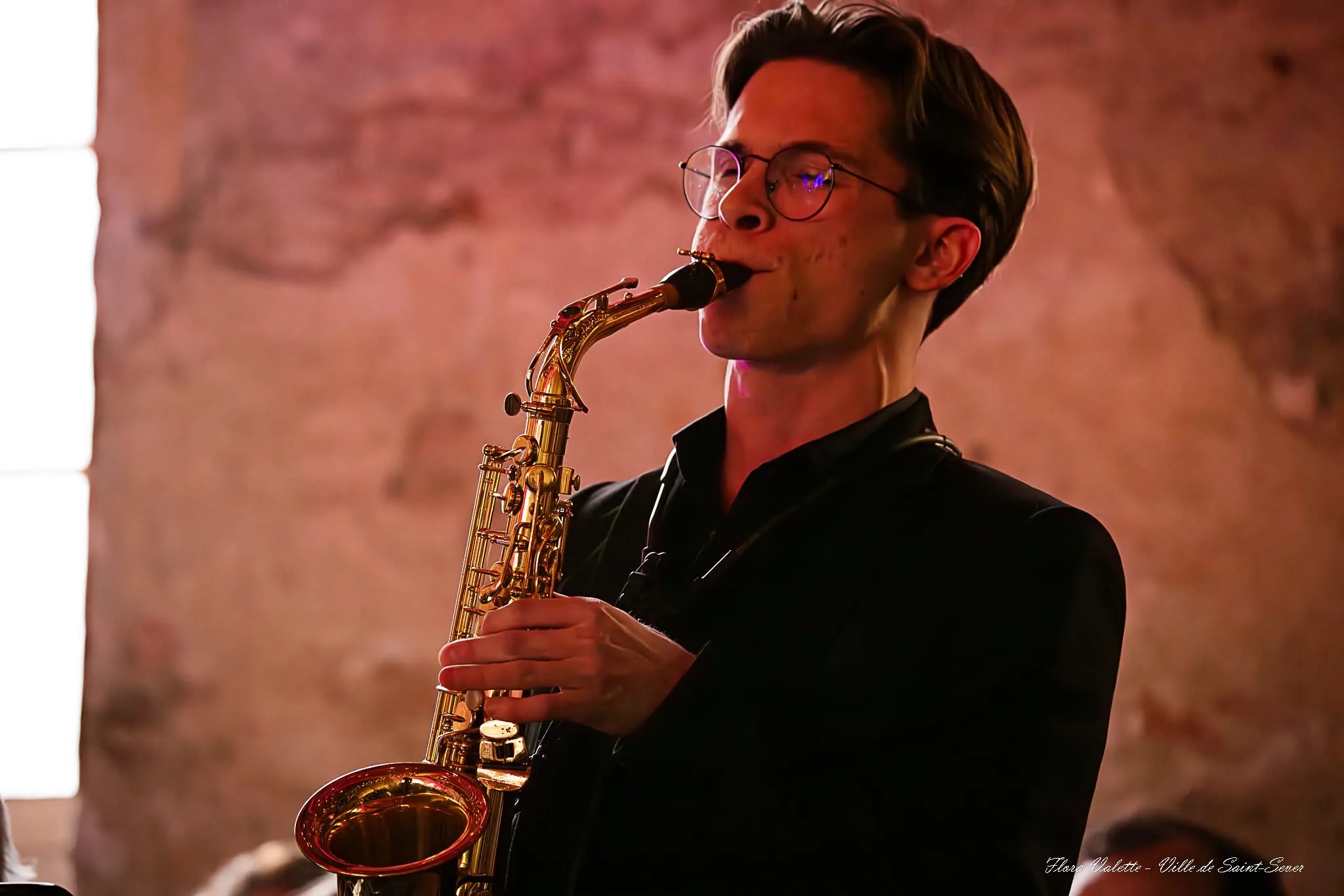 Saxophoniste alto de l'Harmonie du Cap de Gascogne jouant devant les murs de pierre du Cloître des Jacobins
