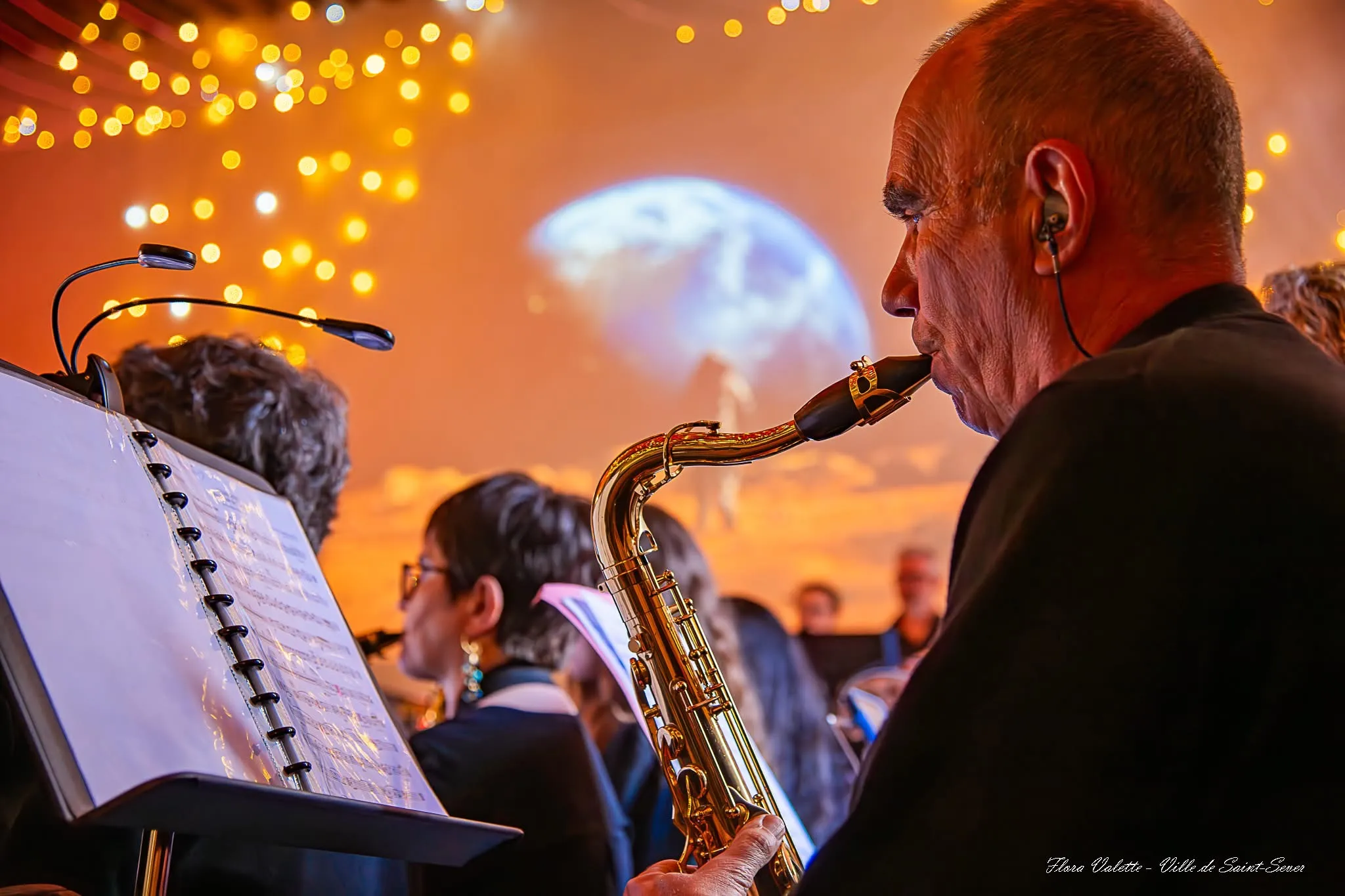 Saxophoniste ténor de dos devant l'écran de projection du concert « On a marché sur Mars », guirlandes lumineuses au plafond